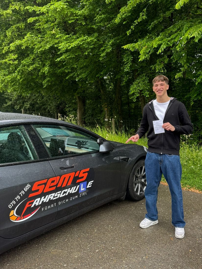 Fahrschüler mit bestandenem Führerschein am Tesla Model 3